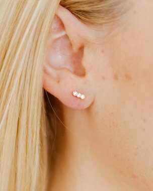 Close-up of a person with blonde hair wearing three small gemstone stud earrings in the earlobe.
