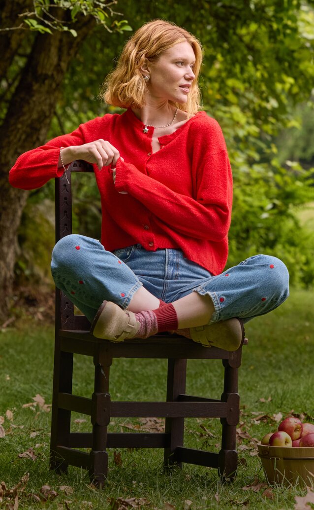 Woman in a red sweater sitting on a chair beside a basket of apples.