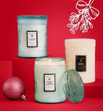 Three candles displayed next to Christmas tree ornaments in front of a red background