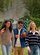 Three friends walk across a grassy lawn carrying a football, wearing casual fall clothing outdoors.