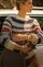 Person standing beside a silver station wagon, wearing a patterned knit sweater and holding a clutch bag in warm outdoor lighting.