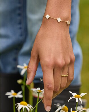 Close-up of a hand wearing a delicate gold clover bracelet and ring.
