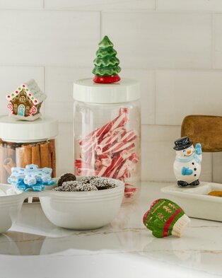 Festive kitchen counter with Nora Fleming Christmas-themed candy jars, holiday treats, and decorative ceramic accents.