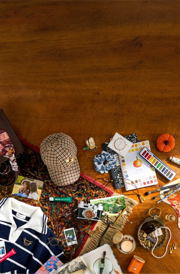 Flat lay of fall-inspired fashion, photos, camera, jewelry, candle, and stationery arranged on a patterned rug and wood table.
