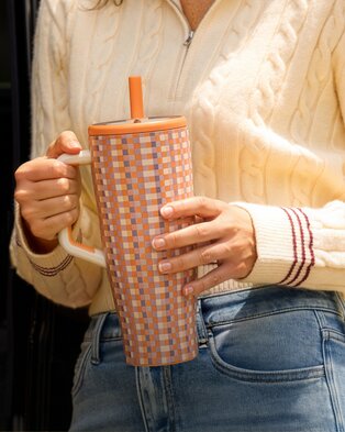 Person holding a patterned insulated tumbler while wearing a cream cable-knit sweater.