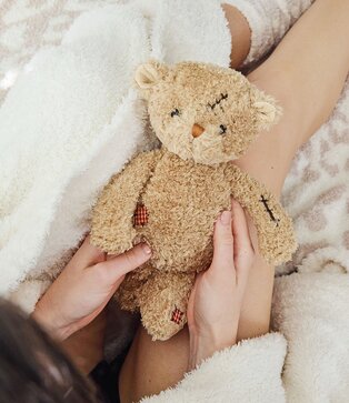 Image of a model holding a Bukowski bear in a cozy robe and blankets
