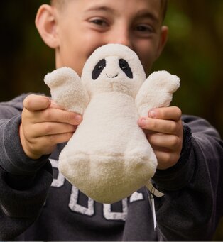 Child holding up a soft white Jellycat ghost plush toy outdoors.