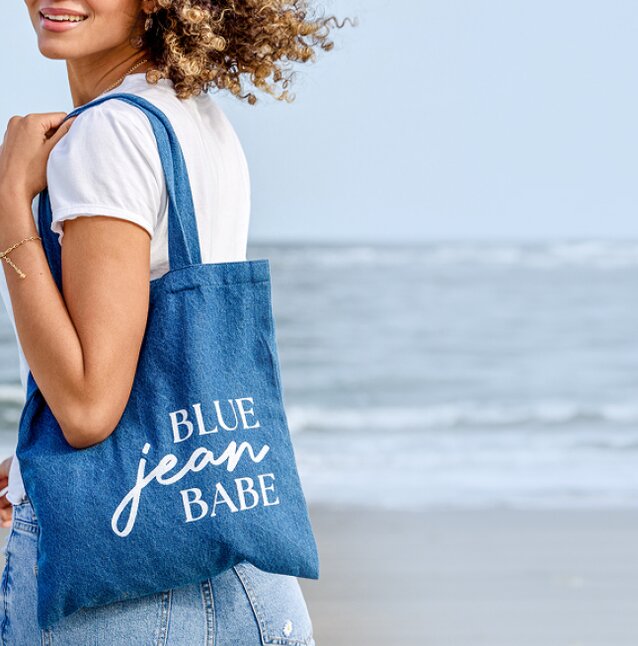 Model holding a denim tote reading "blue jean babe"