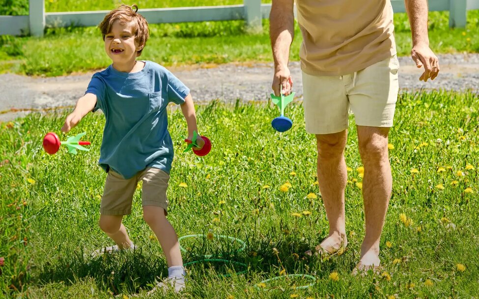 Child playing an outdoor lawn game with an adult in a grassy yard on a bright summer afternoon.