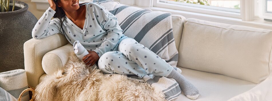 Model lounging on the couch wearing set of pajamas with star motif and fuzzy socks, holding an Owala water bottle