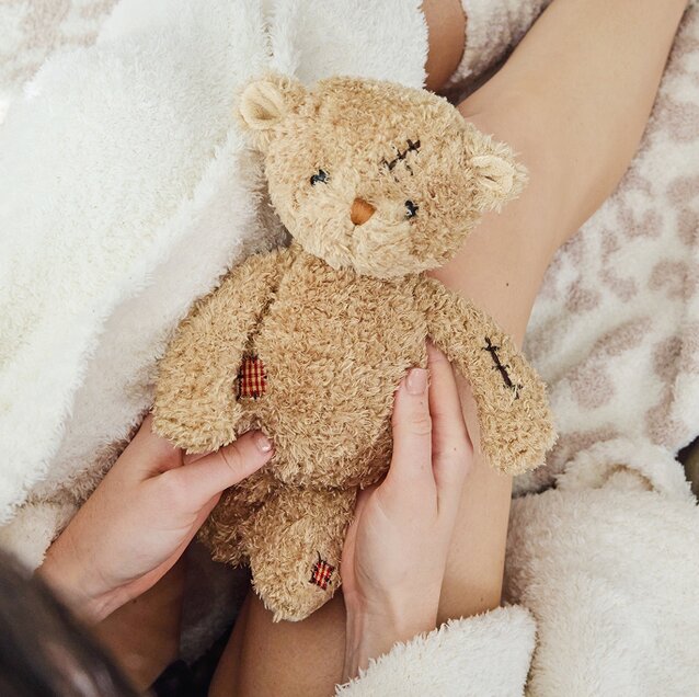 Image of a model holding a Bukowski bear in a cozy robe and blankets