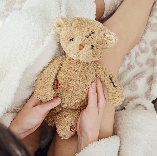 Image of a model holding a Bukowski bear in a cozy robe and blankets