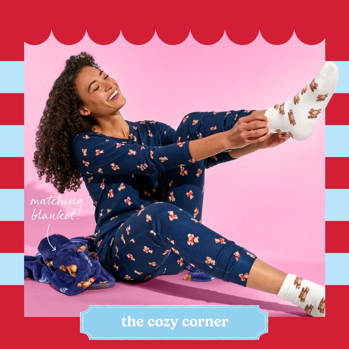 Image of a girl wearing navy blue Christmas pajamas with teddy bears on them, with a matching blanket and socks
