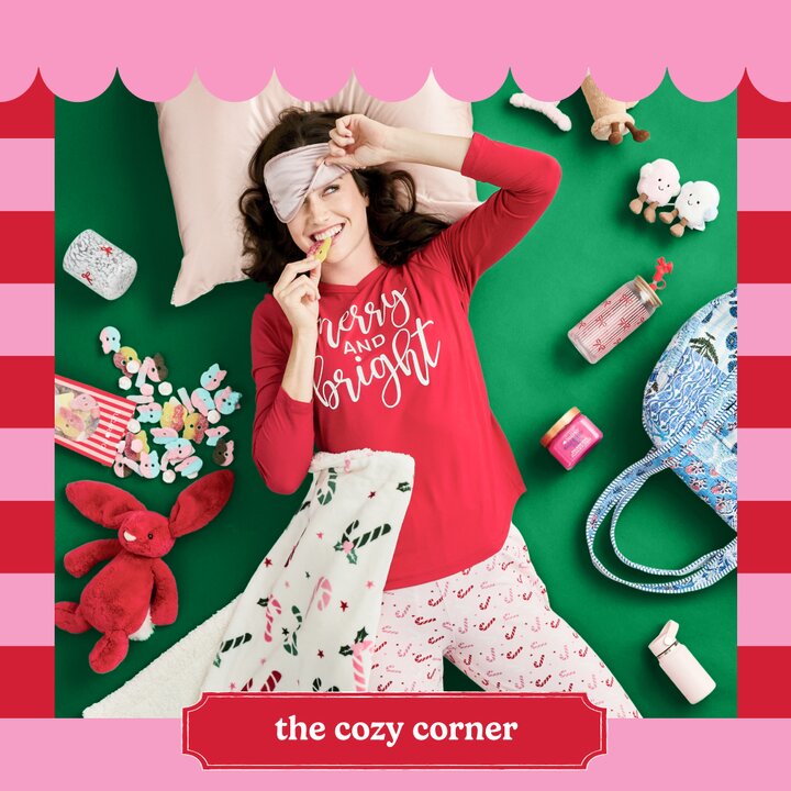 Image of a girl wearing Christmas pajamas lying on a green background, surrounded by gift items including a red plush stuffed bunny, candy, beauty products, a quilted bag, and other items