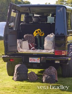 Open trunk of a black SUV filled with Vera Bradley bags and fall tailgate gear. 25% off Vera Bradley travel styles in store and online.