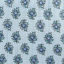 Close-up of a quilted fabric with a repeating small floral motif in blue and navy on a pale blue background. Vertical stitched lines run through the fabric, and a narrow blue-and-white striped binding borders the top edge.