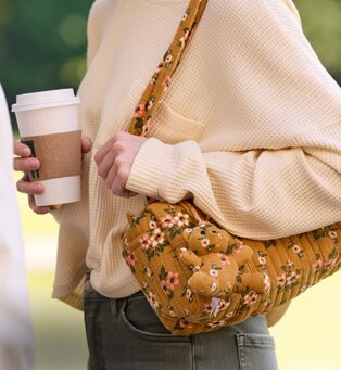 Person carrying a floral crossbody bag while holding a coffee cup.