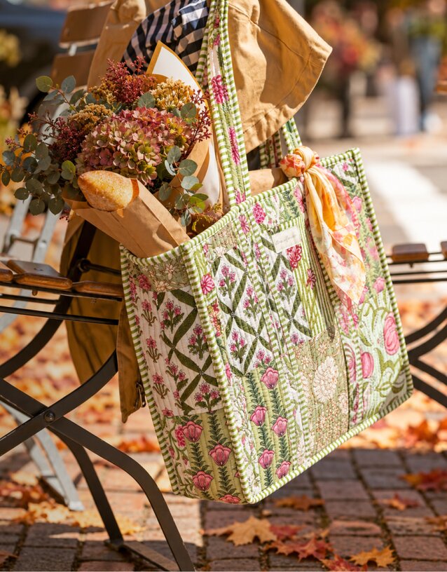 Two floral patchwork quilted tote bags styled for fall, one filled with flowers and a baguette on a park bench, and the other carried by a woman in a cozy coat and scarf by the water.