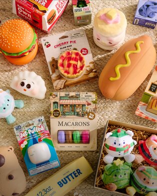 Assortment of food-themed squishy toys, including a hamburger, hot dog, cherry pie, macarons, and holiday plush characters.
