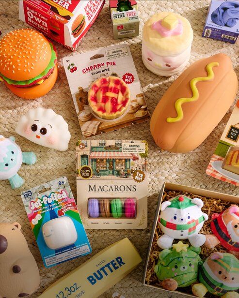 Assortment of food-themed squishy toys, including a hamburger, hot dog, cherry pie, macarons, and holiday plush characters.