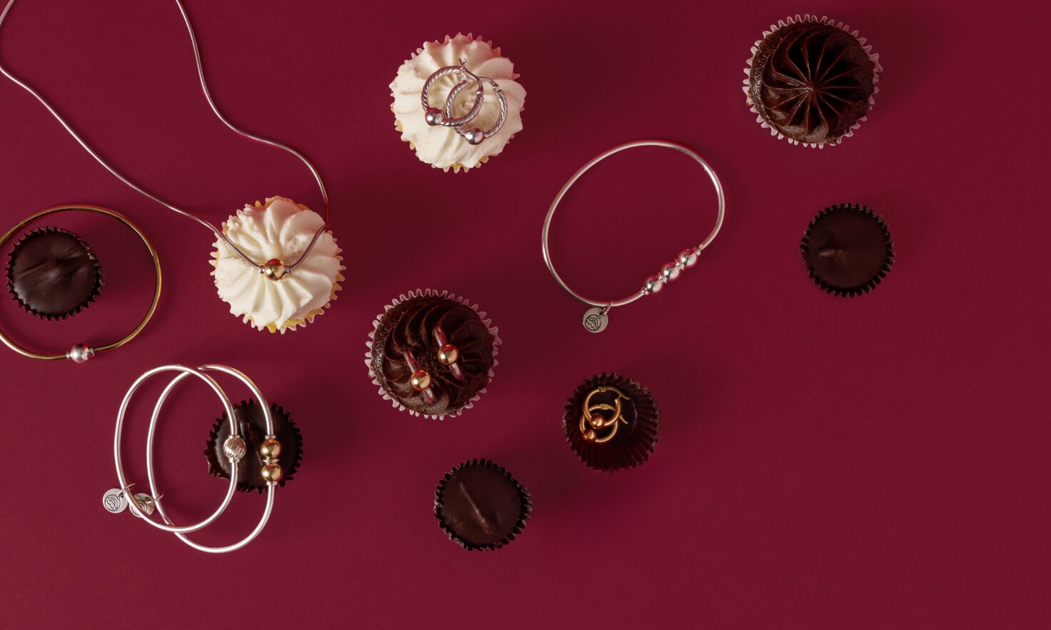 Imag of Cape Cod Jewelry pieces on a berry colored backdrop among valentine's day candies and cupcakes. featuring the classic Cape Cod single, double and triple ball bracelets, single ball neckalce, and single ball earrings.