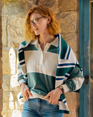 Woman wearing a striped rugby shirt with a coordinating sweater draped over her shoulders.