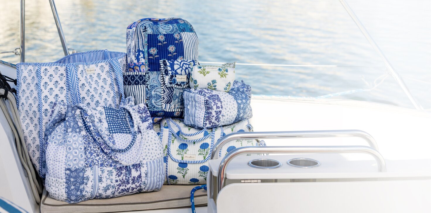 Three overlapping instant photos placed on folded blue-and-white striped and denim fabrics. The center photo shows a smiling woman sitting on a sailboat in a navy top and light blue sailboat-print jeans, shading her eyes from the sun. The left photo shows a cropped view of someone in a navy sweater and flared jeans standing barefoot on a dock, and the right photo shows a person in a pink sweater and jeans sitting on a boat seat by the water.