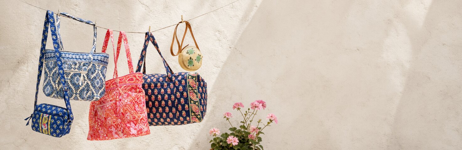 Various Vera Bradley Totes, a Duffel and two crossbodies hanging from a clothesline against a stucco wall