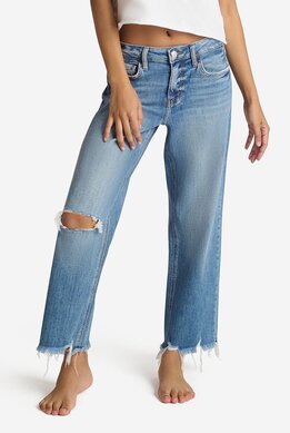 waist-down image of model wearing medium wash relaxed fit jeans with distressed hem and rip at the knee