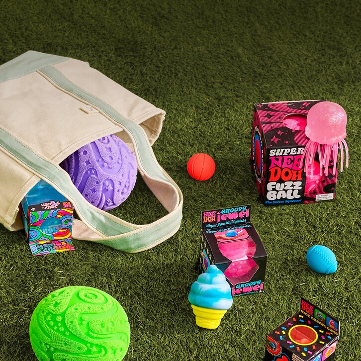 Image of various NeeDoh toys spilling out of a tote onto the grass