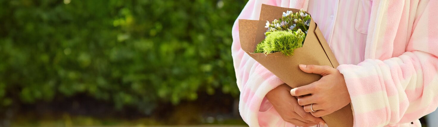 Crop in of a woman in a pink and white striped bathrobe holding a bouquet of flowers