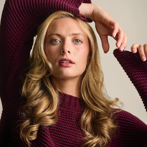 Close-up image of a woman with long blonde hair wearing a cranberry colored knit sweater
