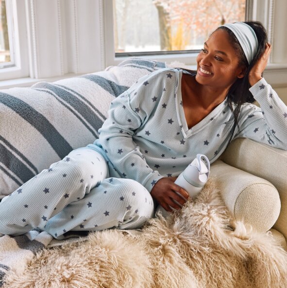 Model lounging on the couch wearing set of pajamas with star motif and fuzzy socks, holding an Owala water bottle