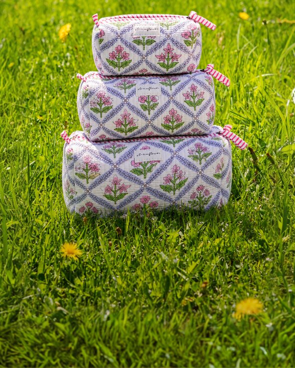 Strawberry-print quilted Strawflower set of 3 cosmetic pouches and fresh strawberries arranged in tall green grass on a bright summer day.