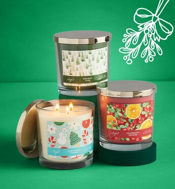 Three candles displayed next to Christmas tree ornaments in front of a green background