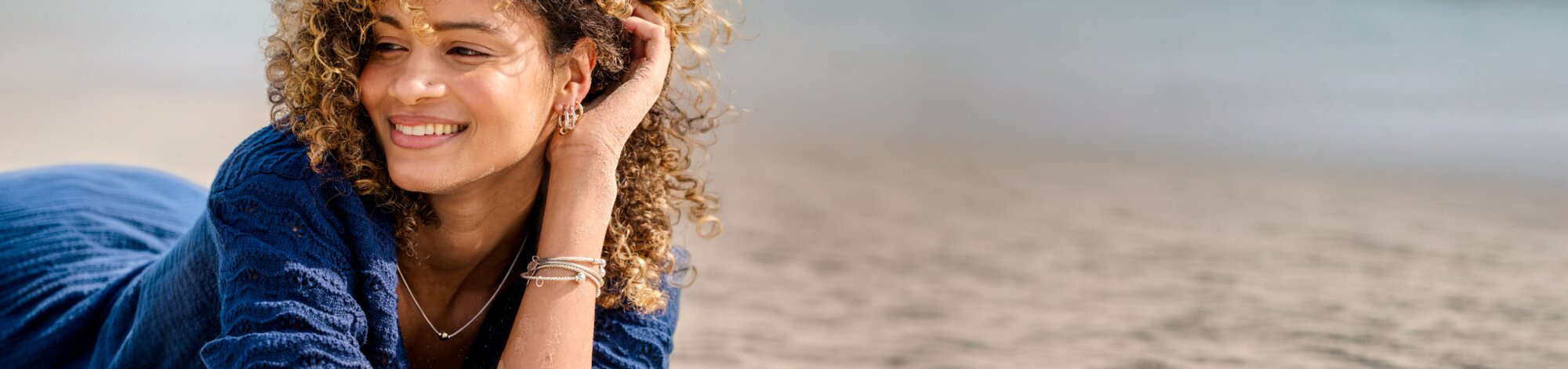 Woman wearing Cape Cod Jewelry bracelets, earrings, and necklace while relaxing on a beach.