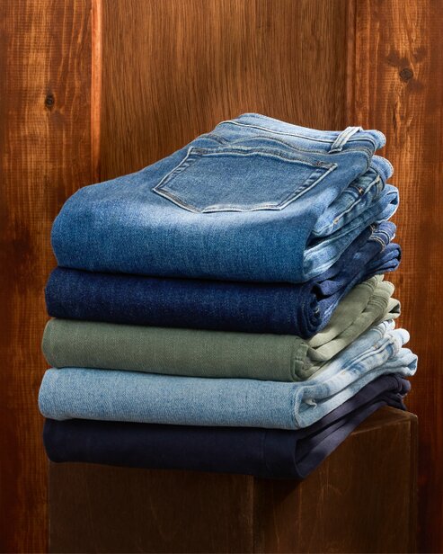 Stack of folded jeans in assorted blue and green washes.