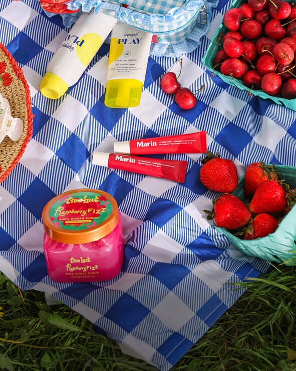 Summer beauty and spa products featuring Supergoop!, Marin and Tree Hut, styled on a picnic blanket with strawberries and seasonal accessories.
