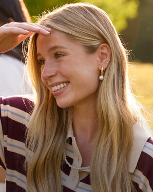 Smiling person wearing pearl earrings and a striped rugby shirt outdoors.