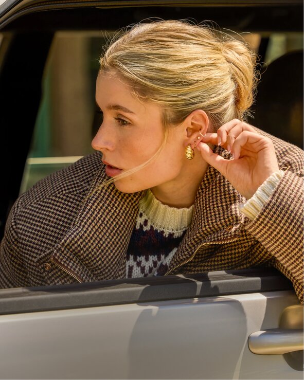 Person putting on gold earrings while seated in a car. Shop jewelry.
