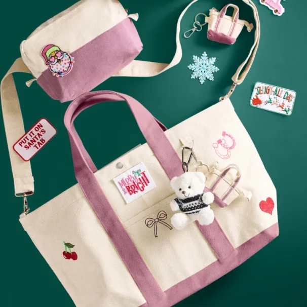 Image of a medium sized cream and pink canvas tote bag and canvas cosmetic pouch decorated with embroidered patches, pins, and a plush bear keychain 