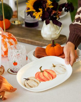 Fall table setting with pumpkin décor, floral arrangement, and painted pumpkin serving platter.