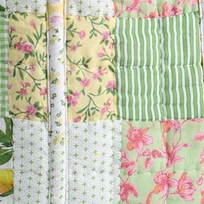 Close-up of a quilted patchwork fabric featuring soft green and yellow squares with floral prints, stripes, and small cross patterns.