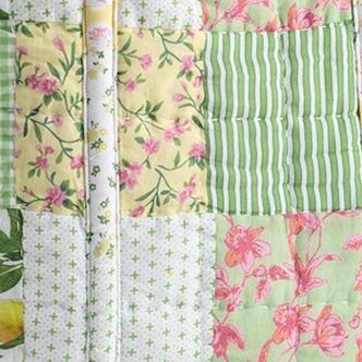 Close-up of a quilted patchwork fabric featuring soft green and yellow squares with floral prints, stripes, and small cross patterns.