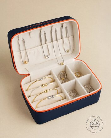 Open navy blue jewelry box with orange trim displaying rings, bracelets, and earrings inside