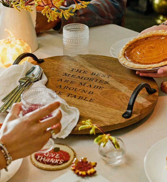 Festive Thanksgiving table setting featuring a wooden serving tray, pumpkin pie, autumn flowers, and seasonal decorations.