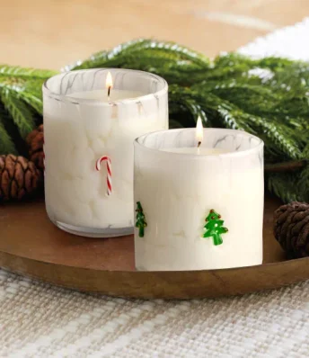 Two holiday candles with Christmas tree designs and candy cane designs on a wooden table top