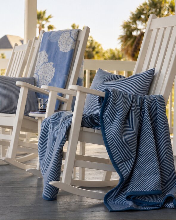 White wooden rocking chairs arranged on a sunny porch with blue pillows and Chappywrap throw blankets, creating a relaxed coastal setting.