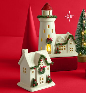 Festive holiday decor houses lit up in front of a red background.