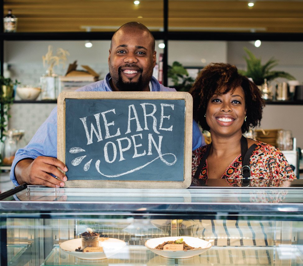 A pair of black business owners holding up a chalkboard reading, "We are open"